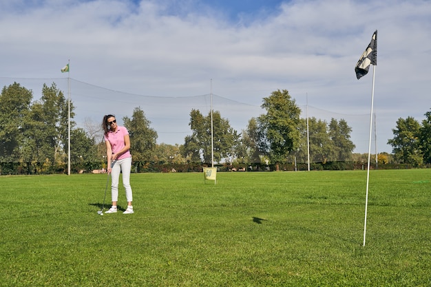 Focused young dark-haired sporty woman using a putter to play golf on the green grass