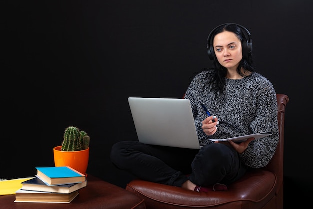 Focused young freelance woman sitting with laptop and headphones working remotely online from home