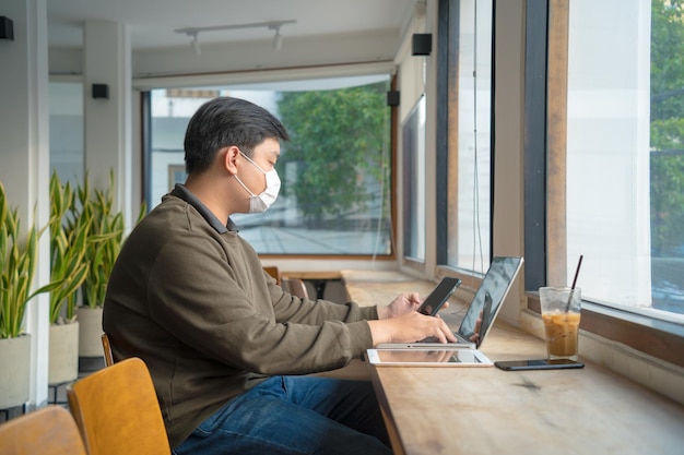 Focused young man wearing a medical mask using laptop typing on keyboard writing email