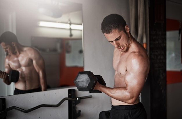 Focusing on his biceps Cropped shot of a handsome and muscular young man working out with a dumbbell in the gym