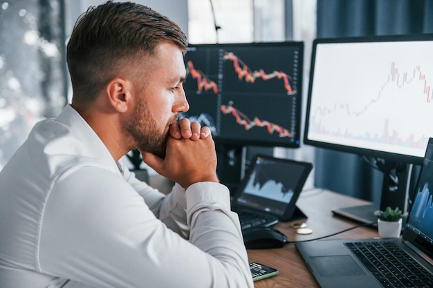 Focusing on the work Young businessman in formal clothes is in office with multiple screens