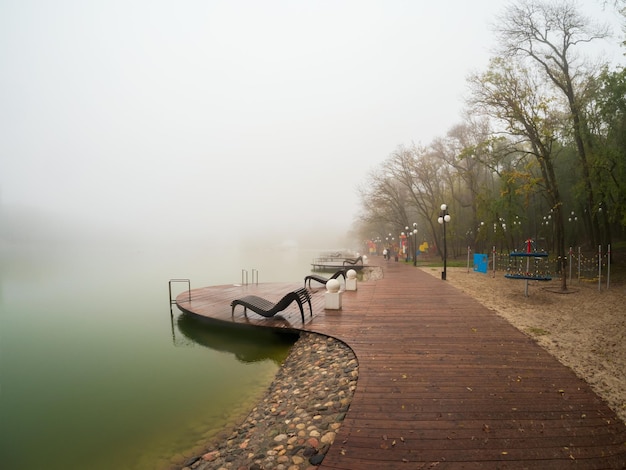 Foggy rainy autumn landscape with modern park in Zheleznovodsk with wooden pier and willow tree under lake Caucasus region Russia