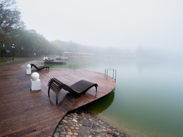 Foggy rainy autumn landscape with modern park in Zheleznovodsk with wooden pier and willow tree under lake Caucasus region Russia