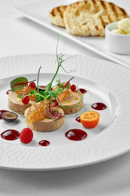 Foie gras with apple confit and berry sauce in a white plate on a white background Closeup selective focus