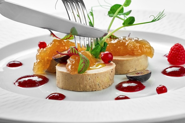 Foie gras with apple confit and berry sauce in a white plate on a white background Closeup selective focus