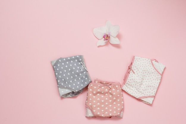 Folded cotton panties of different color with orchid bud on pink background. Woman underwear set. Top view.