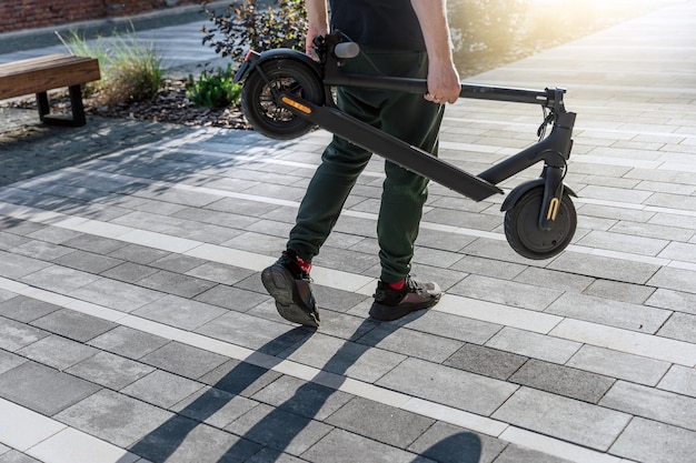 Folded electric scooter in man hand on urban street