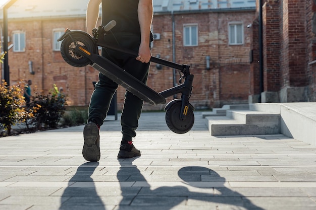 Folded electric scooter in mans hand on urban street