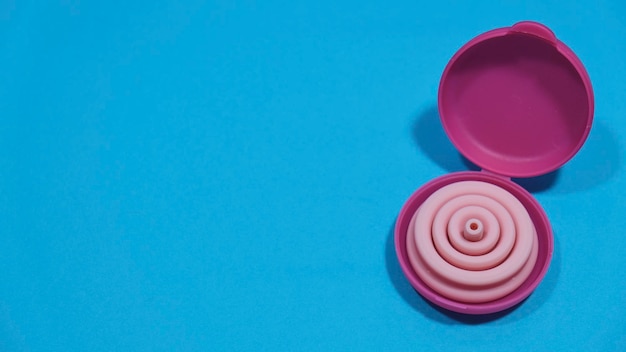 Folded pink menstrual cup in its case on a blue background with copy space