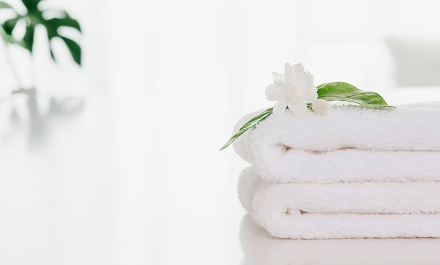 Folded soft terry towel and flower on white table