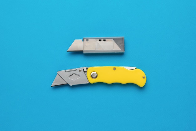 Folding knife for cutting paper and cardboard with a stock of blades on a blue background Flat lay