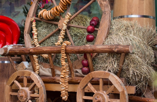 Folk decorations for the Maslenitsa holiday Wooden cart with hay and bagels red apples