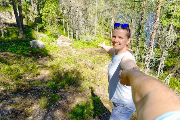 Follow me a beautiful woman holding hands and leads into the forest at summer day