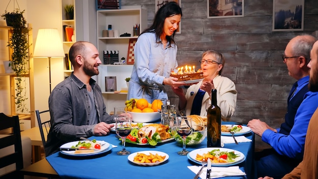 Follow shot of wife with birthday cake for her husband at family dinner.