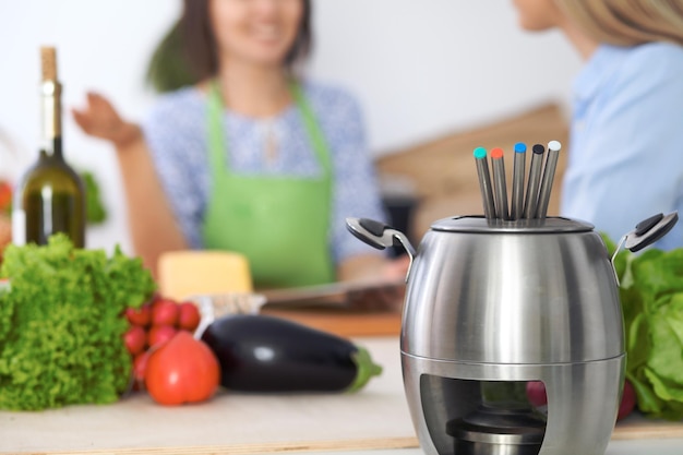 Fondue in a pot at the background of friends cooking together closeup Kitchen interiors and cookware