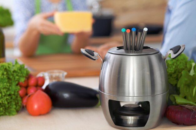 Fondue in a pot at the background of friends cooking together closeup Kitchen interiors and cookware