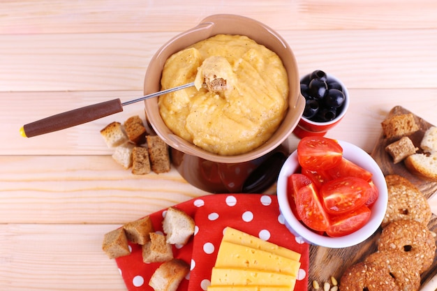 Fondue tomatoes biscuits slices of cheese and rusks on cutting board on polka dot napkin on wooden background