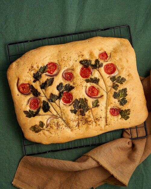 Food art focaccia flatbread with tomatoes on dark green linen textile tablecloth top view