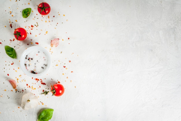 Photo food background. ingredients, greens and spices for cooking lunch, lunch. fresh basil leaves, tomatoes, garlic, onions, salt, pepper. on a white stone table. copyspace top view