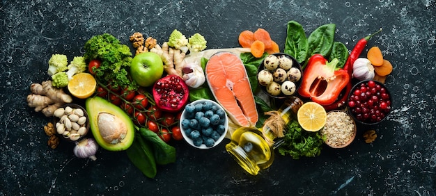 Food background A set of healthy and clean food vegetables fruits fish meat nuts and greens On a black stone background Top view Free copy space