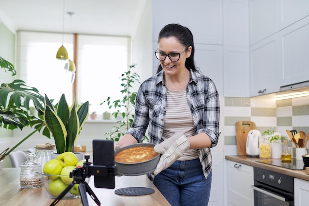 Food blog woman cooking apple pie at home recording recipe on smartphone