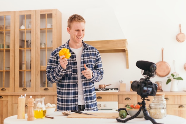 A food blogger creates content and looks at the camera A male cook holds a yellow pepper in his hands and nods at the camera