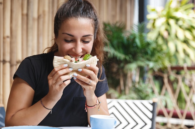 Food blogging and lifestyle concept Portrait of cute european woman eating out at cafe during her travelling tourist trying new cuisine biting pita have lunch at hotel restaurant