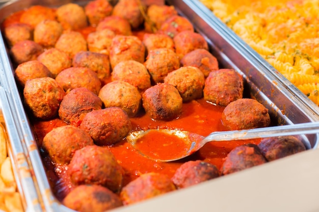 food, catering, self-service and eating concept - close up of meatballs and other dishes on metallic tray