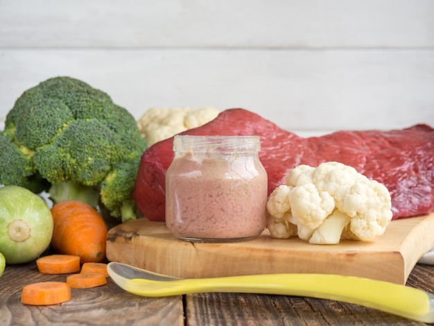 Food for children, baby bait, beef and vegetable puree in small glass jars on rustic wooden background