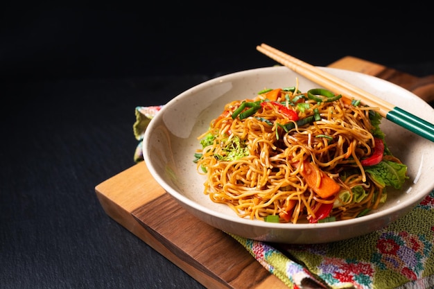 Food concept Asian egg noodles stir fry in ceramic bowl on wooden board with copy space