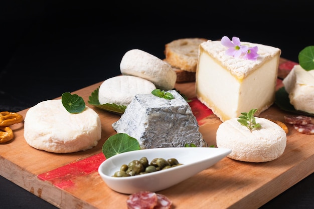 Food concept assortment French organic fresh goat cheese on wooden cheese board on black background with copy space