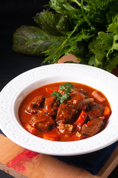 Food concept Homemade French Stew Beef Marengo in white ceramic soup plate on wooden board on black slate stone background with copy space