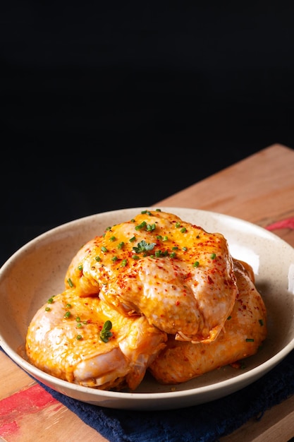 Food concept homemade spicy chicken thighs marinade in ceramic bowl on wooden board with black background and copy space