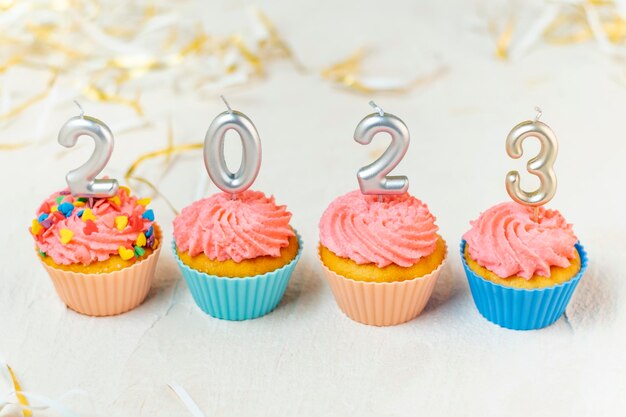 Food concept of New year 2023 Festive cupcakes and candles in form of numbers 2023 on white background