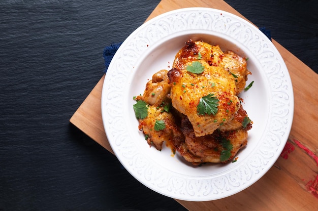 Food concept Roasted spicy chicken thighs on ceramic plate on wooden board with black background with copy space