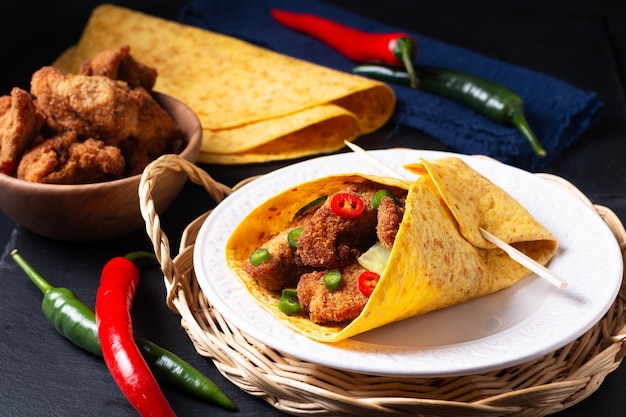 Food concept spicy Fried Chicken Tortilla Wrap with chopped chilies on black slate stone background with copy space