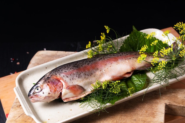 Food concept White Trout fish in in ceramic plate on wooden board on black background with copy space