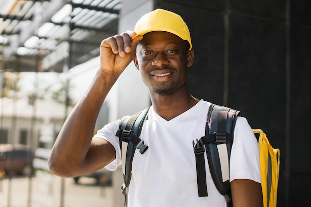 Food delivery portrait of courier african man with yellow backpack and cap