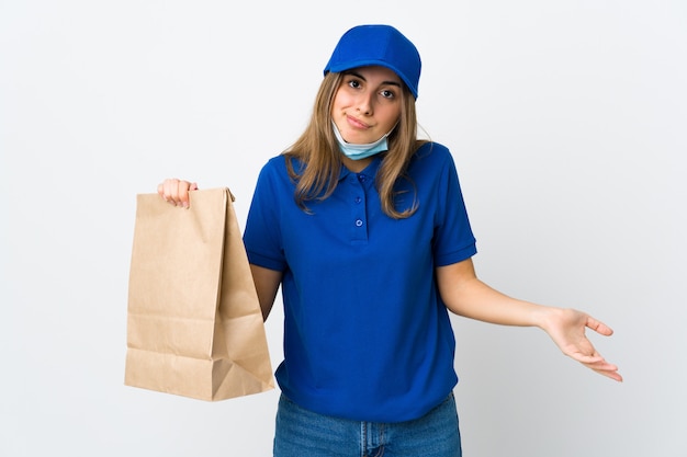 Food delivery woman and protecting from the coronavirus with a mask on isolated white making doubts gesture while lifting the shoulders