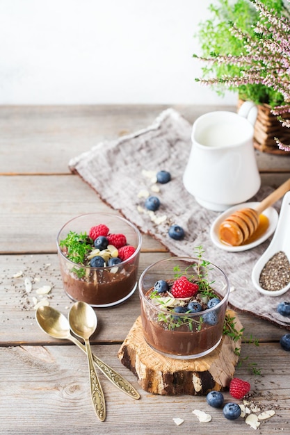 Food and drink healthy eating and dieting concept Homemade chocolate chia pudding with fresh berries and green thyme for breakfast on a cozy kitchen wooden table