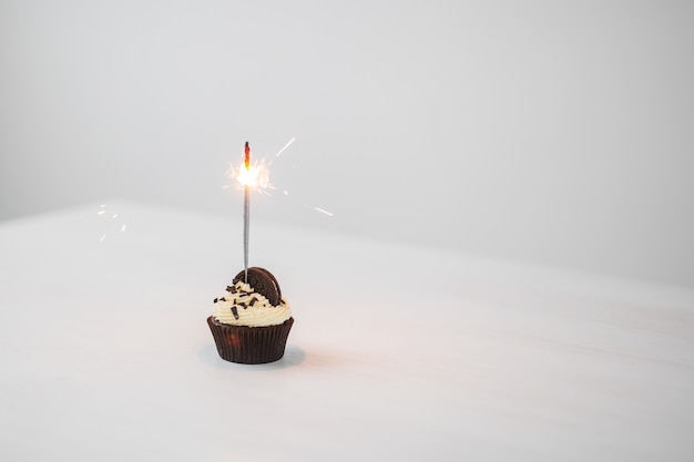 Food and holiday concept - Birthday cupcake with sparkler over white wall with copy space.