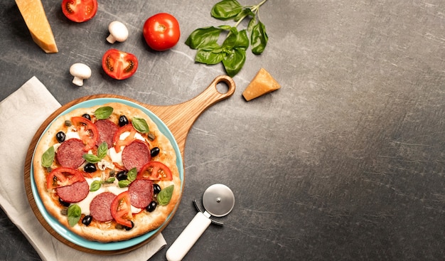 Food ingredients and spices for cooking delicious italian pizza mushrooms, tomatoes, cheese, onion, oil, pepper, salt, basil, olive on black concrete background. Copyspace right. Top view. Banner