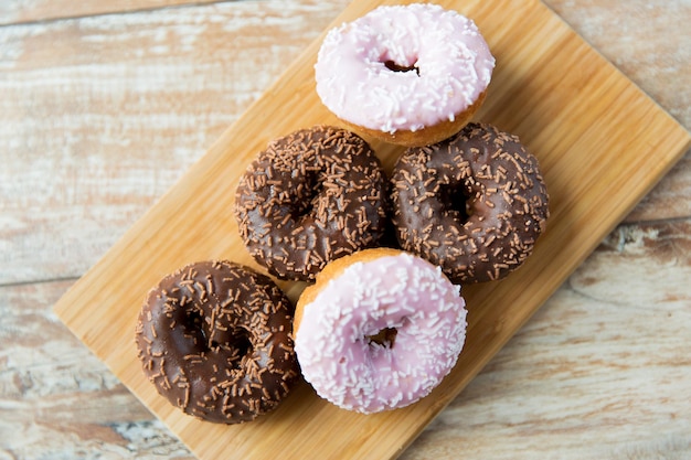 food, junk-food and eating concept - close up of glazed donuts on wooden board