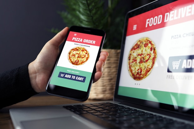 Food online order and delivery app on laptop and phone screens, man at work, business office background. Takeaway food order delivery service application