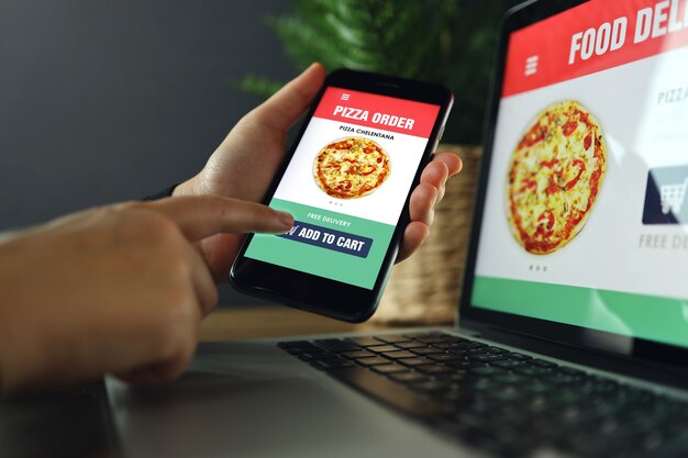 Photo food online order and delivery app on laptop and phone screens, man at work, business office background. takeaway food order delivery service application