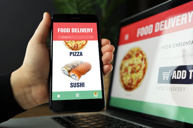 Photo food online order and delivery app on laptop and phone screens, man at work, business office background. takeaway food order delivery service application