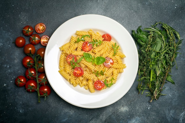 Food pasta on a dark background. Italian fusilli pasta with tomatoes, herbs and basil on a white plate.