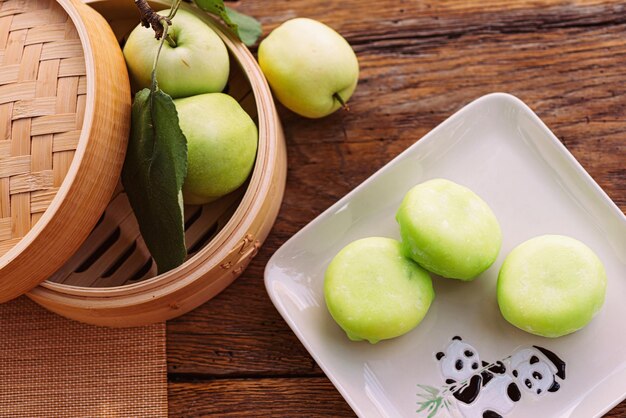 Photo food a plate of green apples next to a basket of apples on a wooden table mochi asian dessert