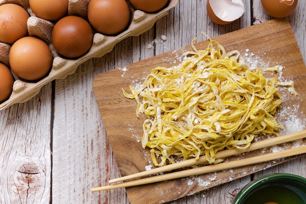 Food preparing - Raw egg noodles   with powder flour on wooden cutting board rounded with eggs