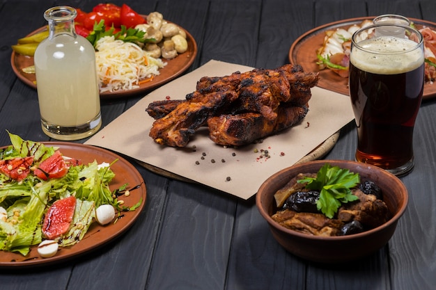 Food set with grilled ribs pickled vegetables bacon salad and moonshine  on black wooden background